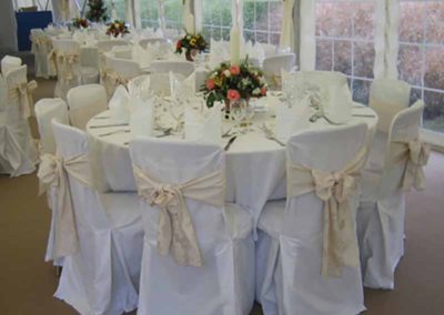 white satin ribbons deck the back of white cloth chairs and a beautiful dressed wedding table