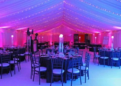 Interior of corporate marquee with black table and chair decor, pink and blue lighting