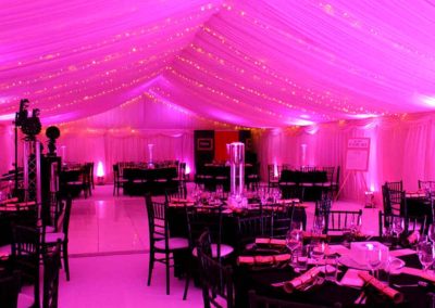 Corporate dinner party marquee, pink lighting, balck linens and chairs at round tables.