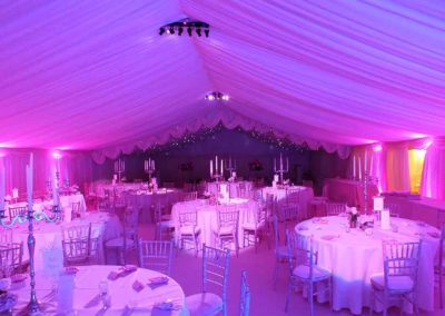 Image of white linens, white banquet chairs, pink lighting, and ceiling swags