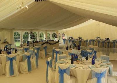 Image of 5ft round tables, white chairs with blue ribbons, starlight LED lighting, ivory swags