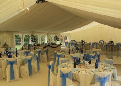 Image of 5ft round tables, white chairs with blue ribbons, starlight LED lighting, ivory swags