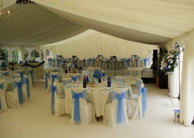 Image of 5ft round tables, white linen table cloths, chair covers with blue ribbons, starlight LED lighting, ivory swags